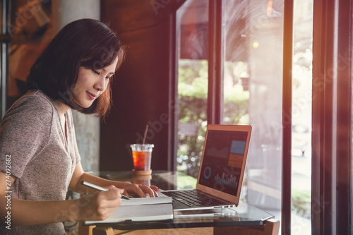 Isolated mockup image of laptop and Young business woman in casual dress sitting at table in cafe and writing in notebook.