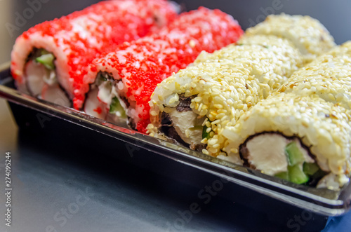Japanese food rolls in a plastic box. A set of kunut covered sushi and red caviar in a plastic box on a black background close-up. Sushi takeaway or sushi delivery.