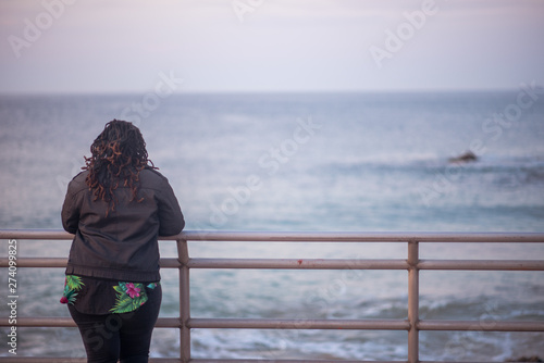 Woman with dreadlocks standing and watching the ocean. Shot from behind