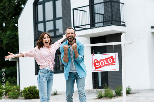 cheerful man and woman celebrating near house and board with sold letters photo