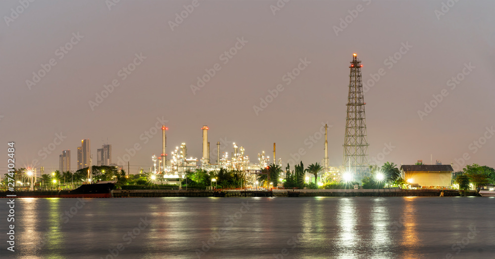 Night photo crude oil refinery plant and many chimney with petrochemical tanker or cargo ship at coast of the river with colorful bright light from lamp reflect on water at thailand