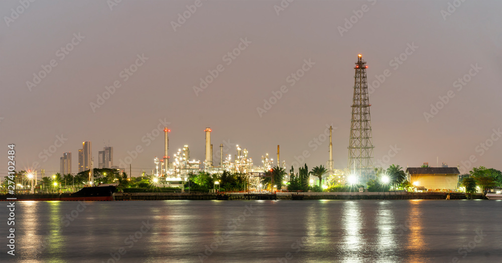Night photo crude oil refinery plant and many chimney with petrochemical tanker or cargo ship at coast of the river with colorful bright light from lamp reflect on water at thailand Night photo crude oil refinery plant and many chimney with petrochemical tanker or cargo ship at coast of the river with colorful bright light from lamp reflect on water at thailand