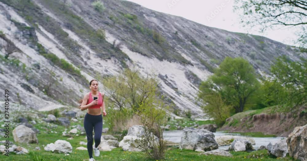 Beautiful lady with a sporty body running through the green field in amazing beautiful place she get tired while she doing her workout stoped then continue her workout while listening music using a Beautiful lady with a sporty body running through the green field in amazing beautiful place she get tired while she doing her workout stoped then continue her workout while listening music using a