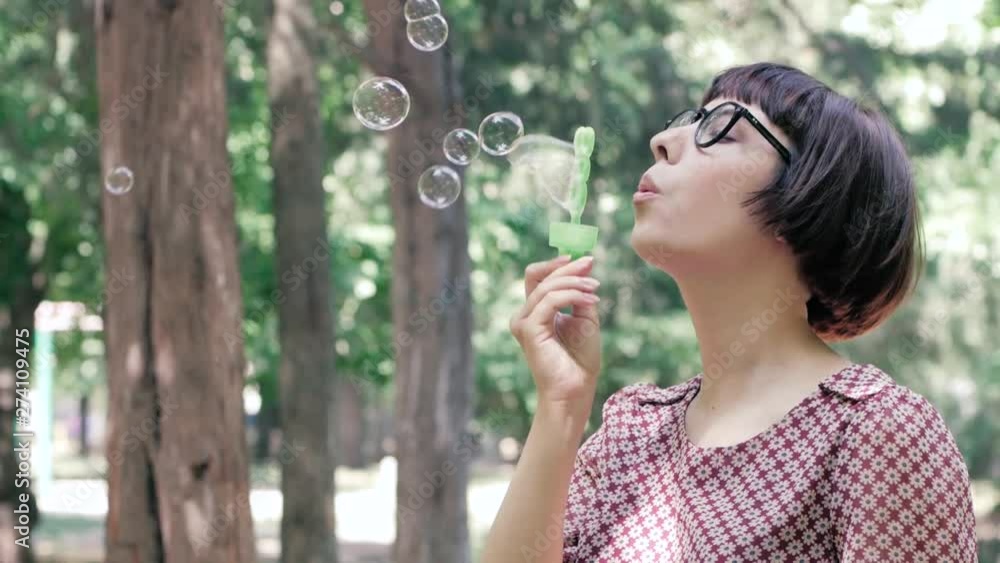 Young woman in glasses blowing bubbles outdoors in the park Young woman in glasses blowing bubbles outdoors in the park