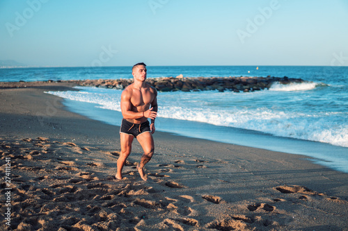 Tattooed bodybuilder sexy male coach at the beach. He runs and shows mucles photo