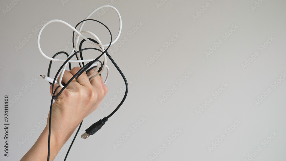 Black and white cables in a left woman's hand on a light gray background Black and white cables in a left woman's hand on a light gray background