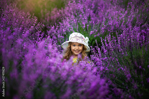 happy baby in a yellow dress in a lavender field throws up a hat and laughs