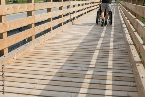 Assistant pushing wheelchair outside in nature on a wooden bridge path