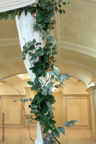 Beautiful wedding huppah decorated with fresh fresh flowers from hydrangea and eucalyptus sheets in a large beautiful wedding hall with a balcony. Wedding floristry photo