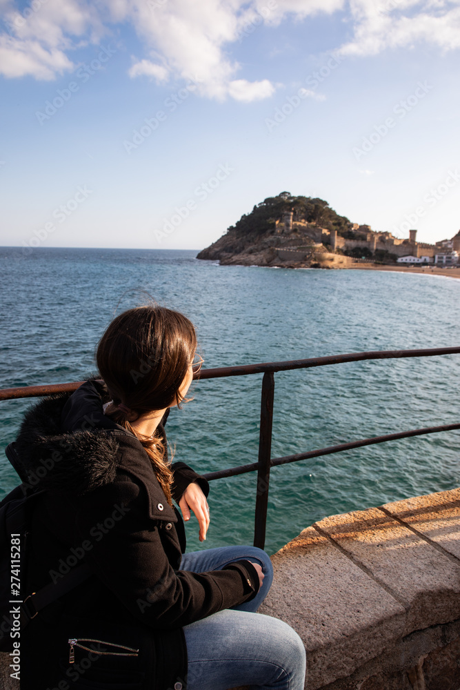 Fototapeta premium Woman watching at medieval fortress on coast near mediterranean town