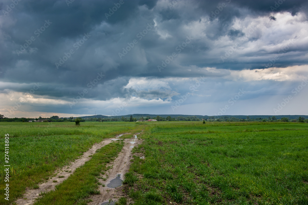 Dirt road through the field and storm clouds in the sky Dirt road through the field and storm clouds in the sky