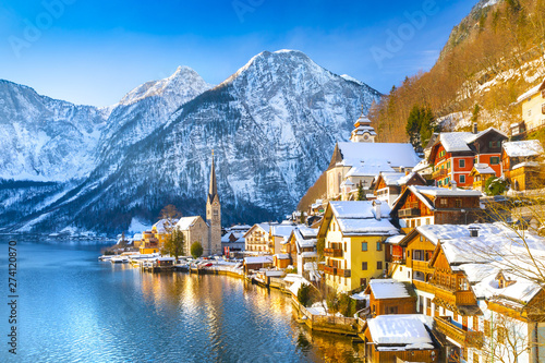 Classic postcard view of famous Hallstatt lakeside town in the Alps with traditional passenger ship on a beautiful cold sunny day with blue sky and clouds in winter, Salzkammergut region, Austria