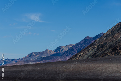 Barren desert landscape with dark volcanic earth and a rugged mountain range receding into the distance - Black Mountains in Death Valley National Park, California