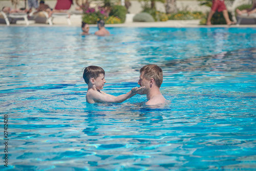 Conscious parenting. Father is teaching his son to swim at the hotel’s pool. © Artem