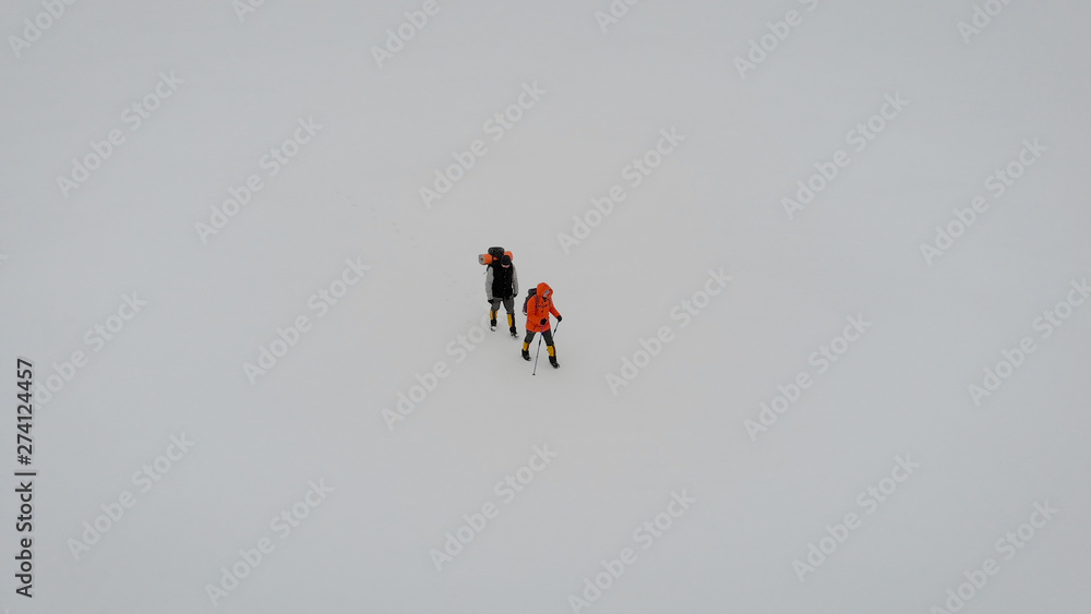 two extreme travelers are strolling over snow field in winter, aerial view, drone is flying over them two extreme travelers are strolling over snow field in winter, aerial view, drone is flying over them