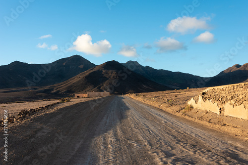 Gravel, dusty road with high volcanic mountains in the background. Morro Jable, Fuerteventura, Canary Islands, Spain. 