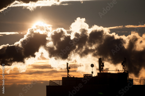 Steam rises from a smokestack on a radiorelay station silhouetted against the sunlight.