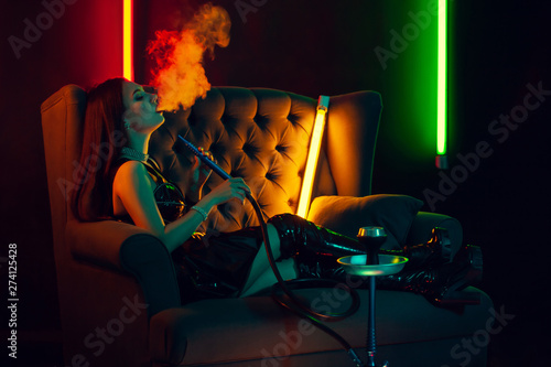 Sexy brunette model is smoking a hookah exhaling a smoke at a luxury night club.