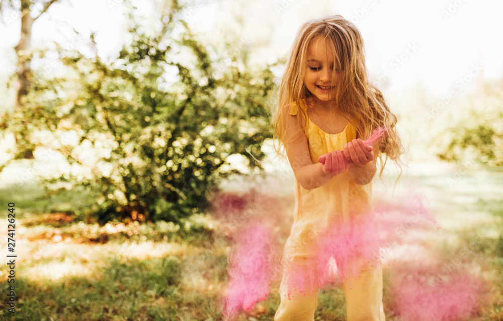 Adorable little girl playing in the park with magical pink dust for an imagination or fairy tale concept. Happy child smiling broadly and playing with pink powder during her birthday party in the park