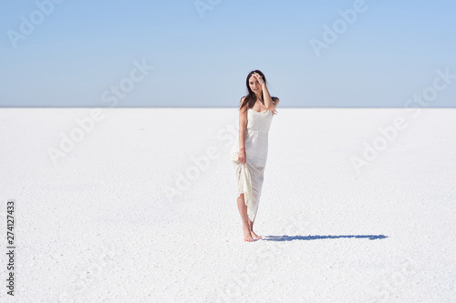 Dark-haired girl in a white dress posing on the dried up salt lake Elton in the Volgograd region in Russia.