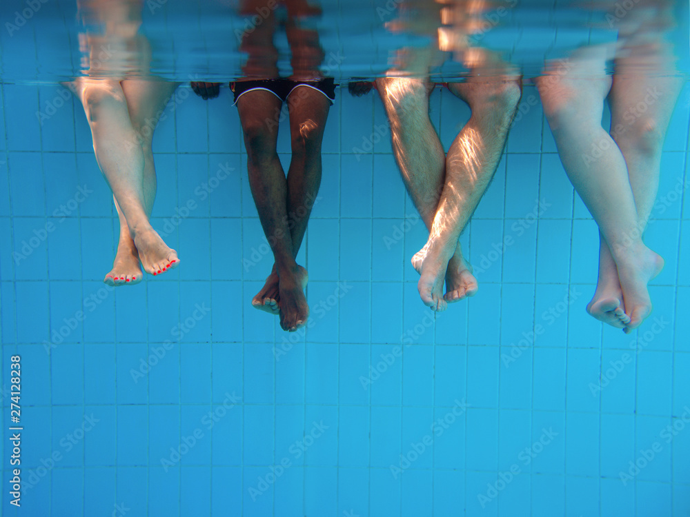four people legs underwater in the swimming pool. Friends. Party. Summer. Vacation and sport concept.