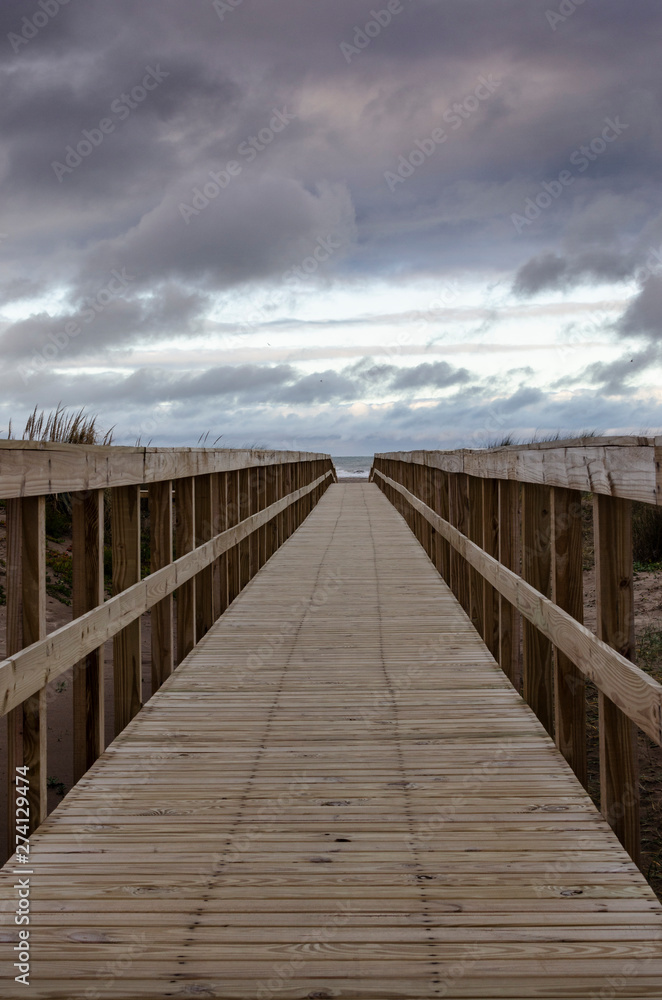 wooden footbridge over the beach in cloudy winter day