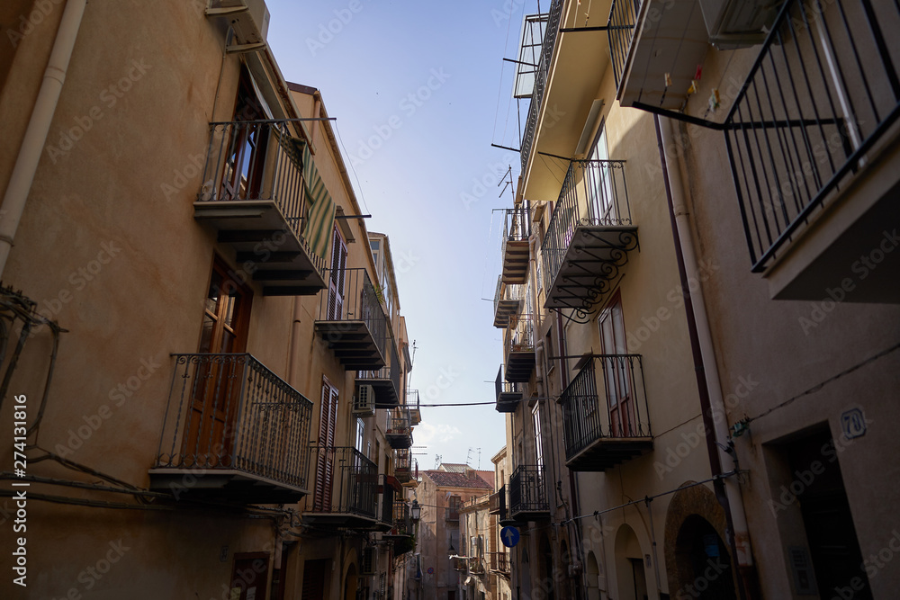 Typical example of historic mediterranean architecture of italian narrow small street in city Cefalu on the island Sicily, houses build from stones with balcony. Picture is taken in sunny spring day.