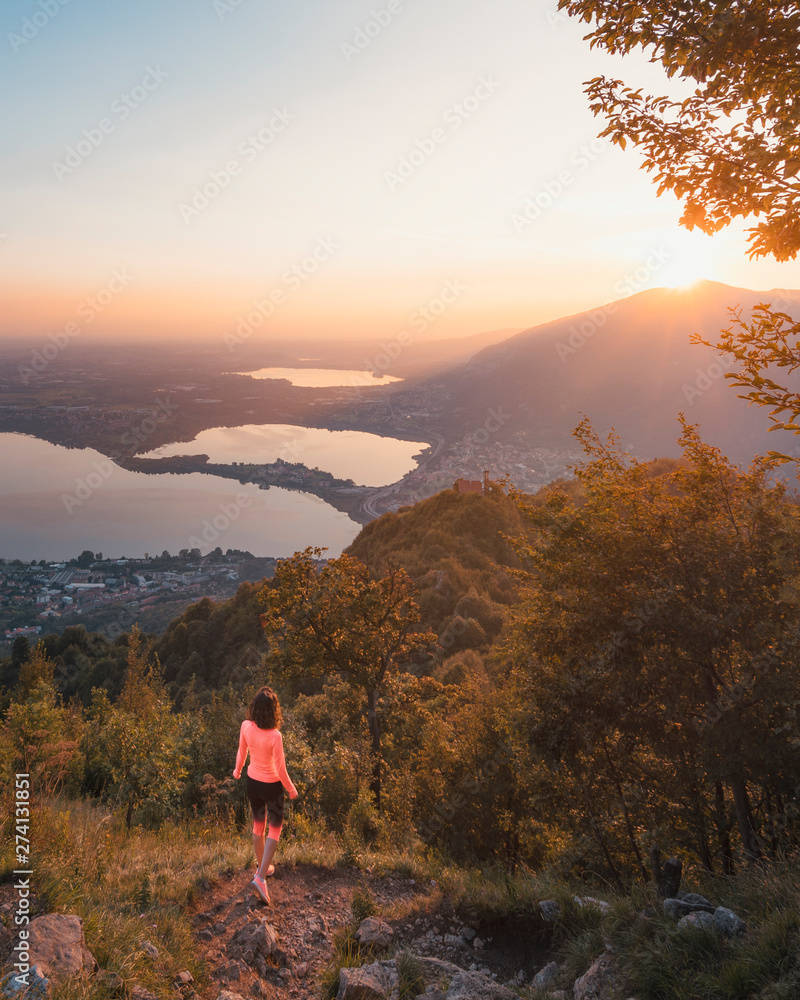 A girl doing jogging on Monte Barro with a view over the Brianza and lake Annone at sunset