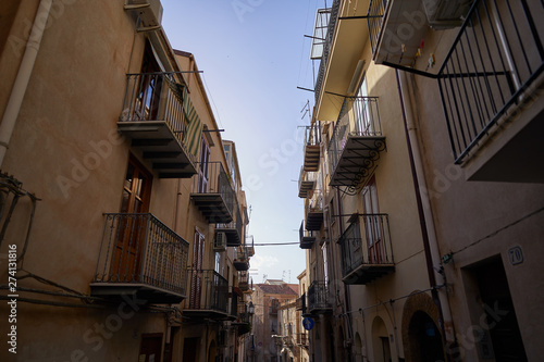 Typical example of historic mediterranean architecture of italian narrow small street in city Cefalu on the island Sicily, houses build from stones with balcony. Picture is taken in sunny spring day.