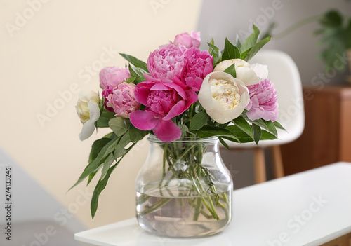 Vase with bouquet of beautiful peonies on table in room