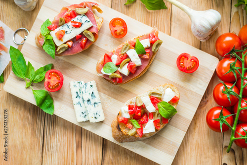 Traditional Italian bruschetta with blue cheese, feta, tomatoes, basil leaves, jamon on a wooden background.