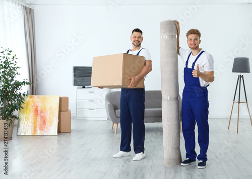 Moving service employees with box and carpet in room