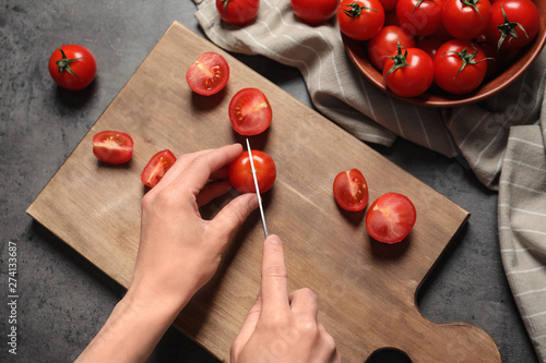 Woman cutting fresh cherry tomatoes on wooden board at table, top view