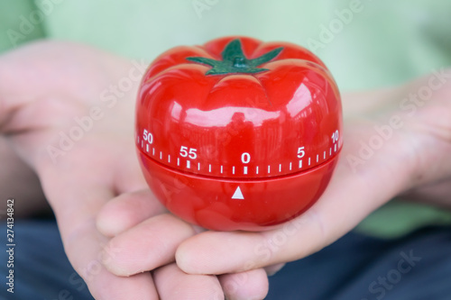 Red tomato kitchen timer set to 0, held by both hands, with open palms