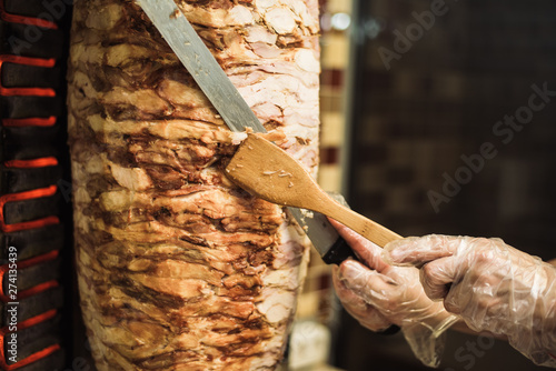 Cooking shawarma and ciabatta in a cafe. A man in disposable gloves cuts meat on a skewer.