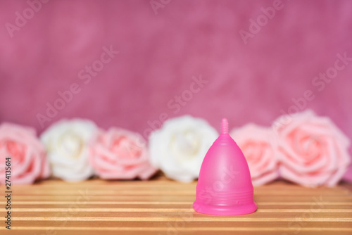 Pink menstrual cup from a medicinal silicone. Pink and white roses decoration. Concept of eco friendly alternative and zero waste solution of intimate hygiene.