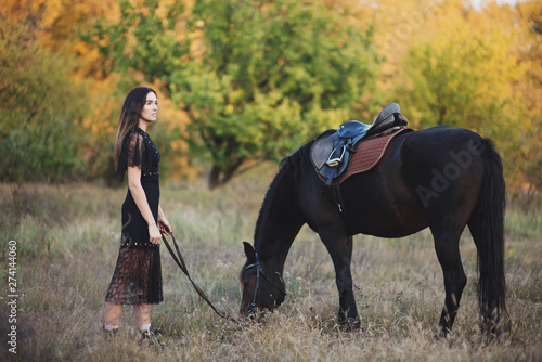 Beautiful woman standing near the horse and holding the rains.