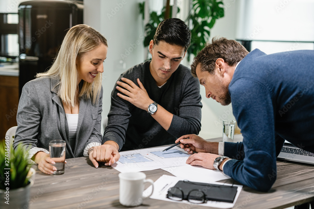Real estate agent and young couple examining blueprints on a meeting. Real estate agent and young couple examining blueprints on a meeting.