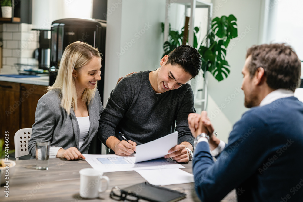 Young happy couple signing mortgage contract on a meeting with real estate agent. Young happy couple signing mortgage contract on a meeting with real estate agent.