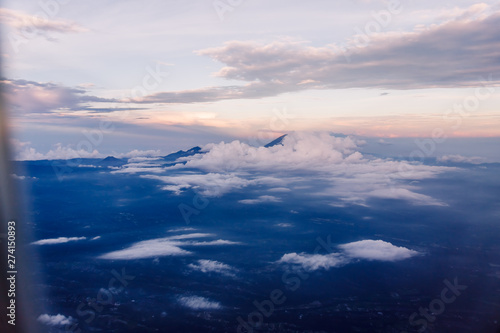 Plane window view with blue sky and beautiful clouds. Clouds and sky as seen through window of an aircraft. View of ocean, city and volcane Agung from the airplane. Aircraft from Thailand to Bali.