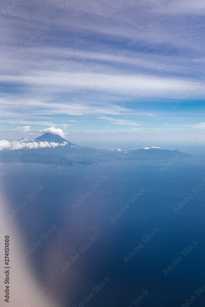 Plane window view with blue sky and beautiful clouds. Clouds and sky as seen through window of an aircraft. View of ocean and volcano Agung. Airplane from island Bali to Labuan Bajo, Komodo.