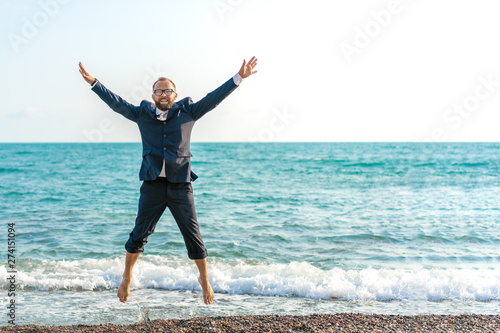 Happy businessman jumping on the beach. Man having fun by the sea. Summer vacation and travel concept