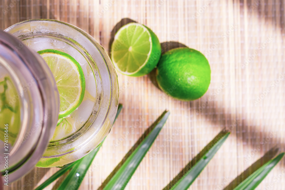 Cold fresh lemonade drink with lime slice and ice cubes in a jar on a tropical background Cold fresh lemonade drink with lime slice and ice cubes in a jar on a tropical background