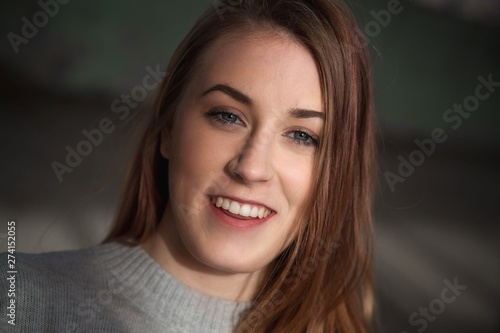 Close-up portrait of cute, redhead teenage girl with blue eyes in gray sweater smiling.