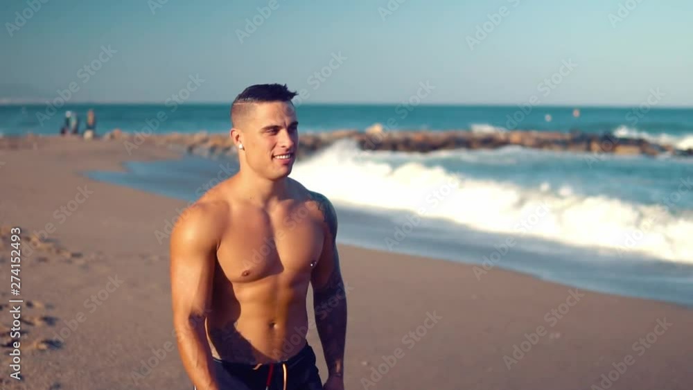 Tattooed bodybuilder sexy male coach at the beach. He walks and shows his muscles Tattooed bodybuilder sexy male coach at the beach. He walks and shows his muscles