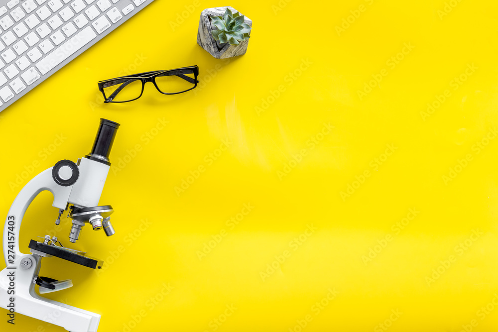 Do medical research on laboratory desk with microscope, keyboard, glasses on yellow background top view mockup Do medical research on laboratory desk with microscope, keyboard, glasses on yellow background top view mockup