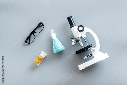 Do medical research with microscope, glasses, test-tubes in lab on gray background top view