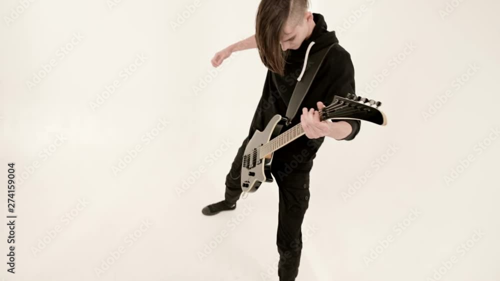 Stylish rhythm guitarist with different eyes in black clothes on a white background expressively playing the black guitar in a white studio Stylish rhythm guitarist with different eyes in black clothes on a white background expressively playing the black guitar in a white studio