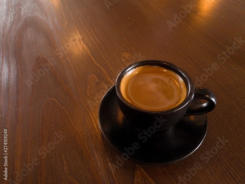 Black coffee mugs and spoon are placed on brown wood