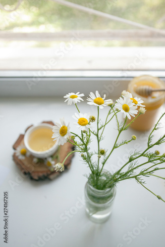 Cup of herbal chamomile tea on a windowsill. Chamomile tea in a whitecup and camomile flowers. Herbal tea for baby's stomach, remedy alternative. Copy space photo